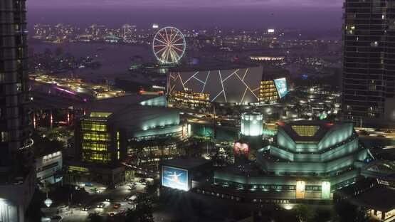 A screenshot from Grand Theft Auto VI (PlayStation 5) shows a vibrant cityscape at night with a lit Ferris wheel and modern buildings.