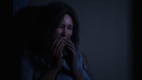 Screenshot from Halloween: The Game showing a distressed woman crouched in a dark corner, lit dimly with an eerie atmosphere.