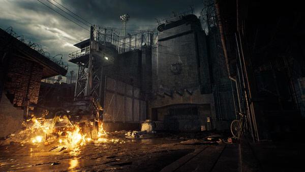 Screenshot from Resident Evil Veronica showing a burning vehicle in front of a fortified building surrounded by barbed wire.