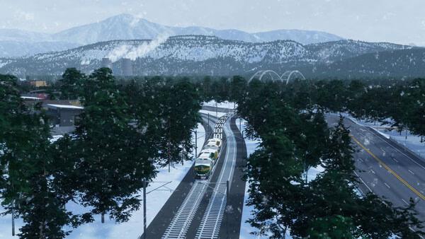 A Cities: Skylines II screenshot showing a snowy landscape with a train on tracks, a highway, and mountains in the background.