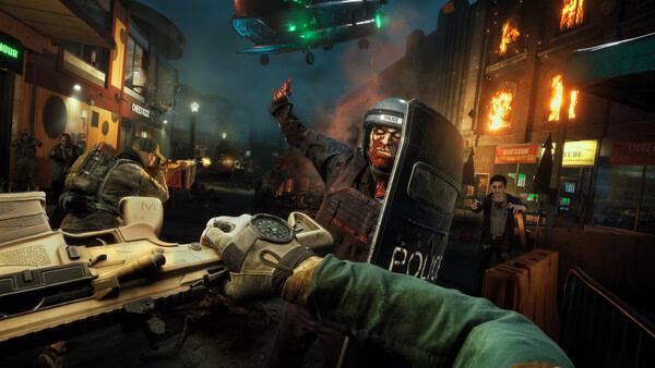 A "No More Room in Hell 2" screenshot showing a chaotic street fight against zombies, with fire, a soldier, and a police zombie in focus.