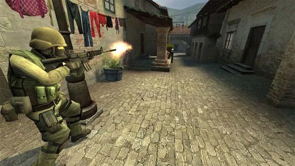 A Counter-Strike: Source screenshot showing a soldier firing a rifle in a cobblestone alley with buildings and hanging laundry.