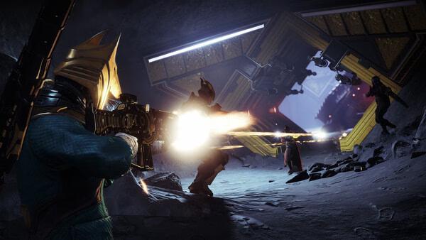 A Destiny 2 screenshot showing a Guardian in golden armor firing a rifle at enemies in a sci-fi cave with glowing structures.