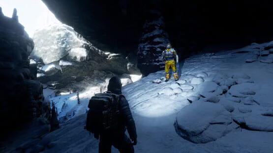 Permafrost screenshot: Two explorers in snowy cave, one in yellow gear standing under sunlight, the other in shadow with a backpack.