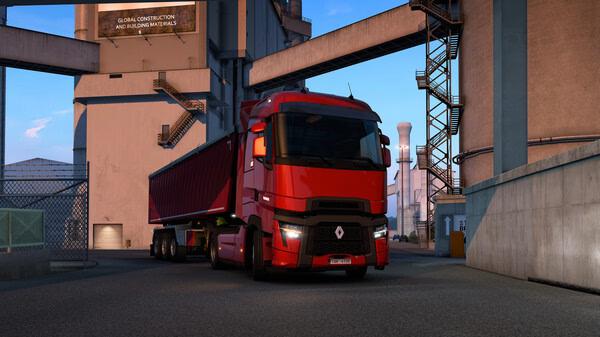 Euro Truck Simulator 2 screenshot: A red truck with a trailer parked near industrial buildings under a clear blue sky.