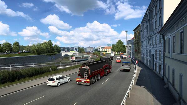 Screenshot of Euro Truck Simulator 2 showing a tanker truck driving on a busy city road with cars, buildings, and a bridge in the background.