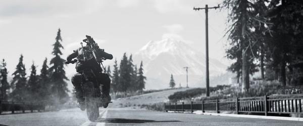 A Days Gone screenshot showing a biker speeding down a deserted road with mountains in the background.