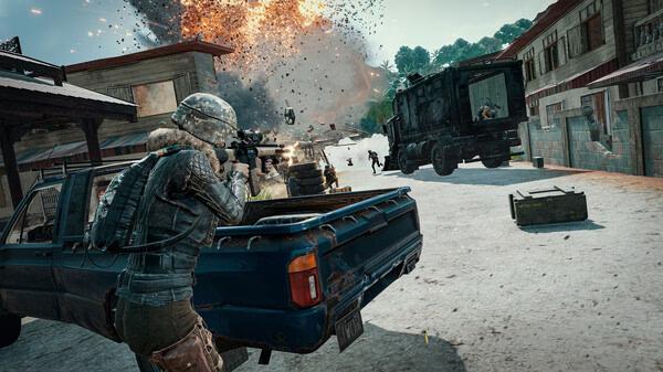 A PUBG: BATTLEGROUNDS screenshot showing a player aiming a rifle from a truck's bed as an explosion occurs in a village street.