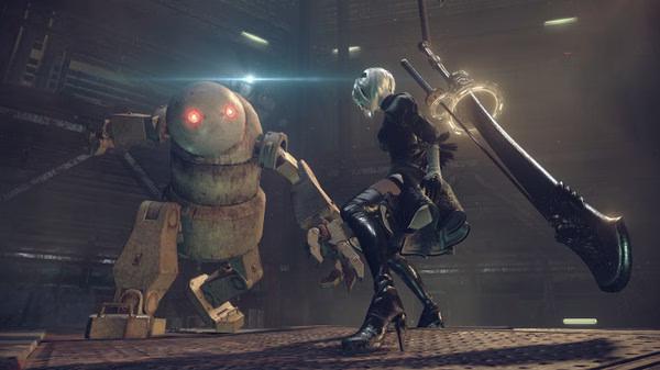 Screenshot from NieR:Automata™ showing a character wielding a large sword facing a robot in a dimly lit industrial setting.