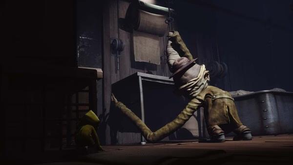 Screenshot of Little Nightmares showing a small character in a yellow raincoat hiding from a tall, lurking creature in a dimly lit room.