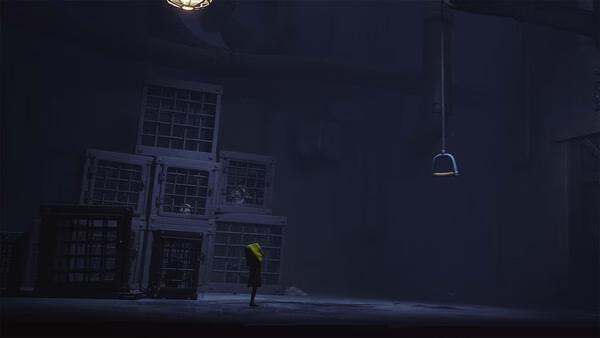 Screenshot from Little Nightmares showing a small figure in a yellow raincoat standing near stacked cages in a dimly lit room.