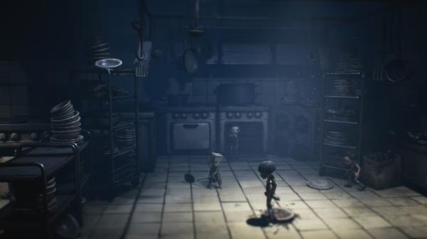 Little Nightmares II screenshot: Two characters navigate a dimly lit kitchen filled with stacked plates and hanging utensils.