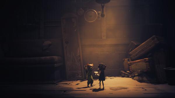 Screenshot from Little Nightmares III showing two small characters in a dimly lit room filled with old furniture and shadows.