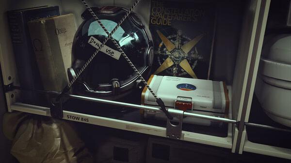 Starfield screenshot: A shelf holding a helmet labeled "DMV USE", books, and a device, with a guidebook visible in the background.