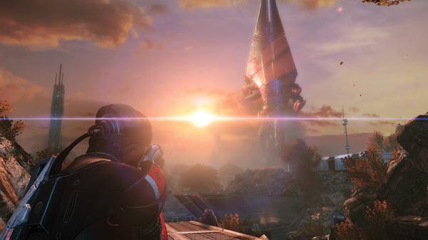 A screenshot from Mass Effect™ Legendary Edition shows a soldier gazing at a towering structure during a vibrant sunset.