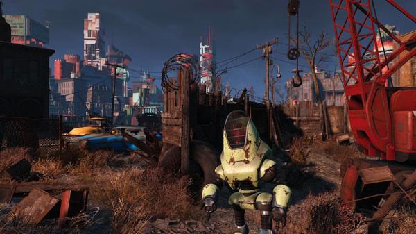 A Fallout 4 screenshot showing a green robot in a post-apocalyptic junkyard with buildings visible in the background.
