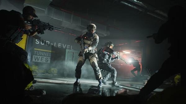 Screenshot from Battlefield™ 2042 showing soldiers in tactical gear advancing through a dimly lit industrial corridor.