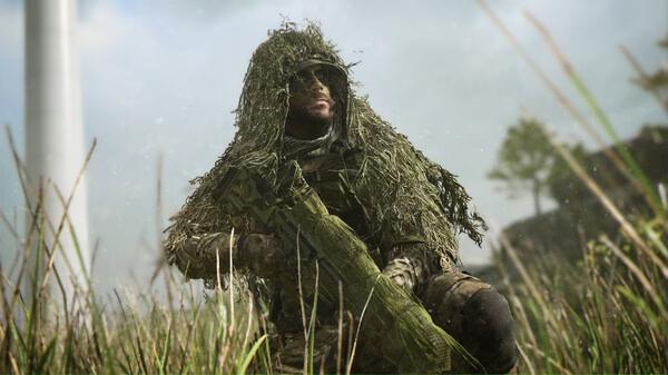 A Call of Duty®: Modern Warfare® II screenshot shows a soldier in a ghillie suit crouched in tall grass, holding a weapon.