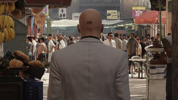 HITMAN World of Assassination screenshot: Agent 47, in a white suit, walks through a bustling outdoor market.
