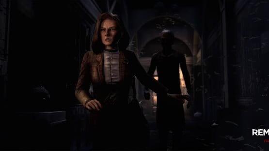 Screenshot from Remothered: Tormented Fathers showing a woman cautiously moving through a dimly lit hallway with a figure behind her.