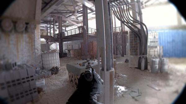 A screenshot from Unrecord showing a first-person view of a gun aimed inside a warehouse with scattered debris and industrial structures.