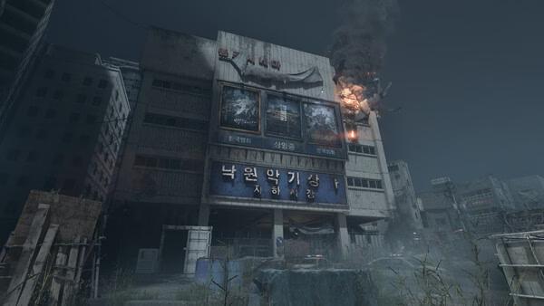 Screenshot from NAKWON: LAST PARADISE showing a dilapidated building with burning debris and fog in a post-apocalyptic setting.