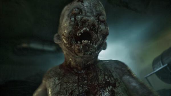 Screenshot from the horror game ILL, showing a grotesque, blood-covered creature with sharp teeth in a dimly lit environment.