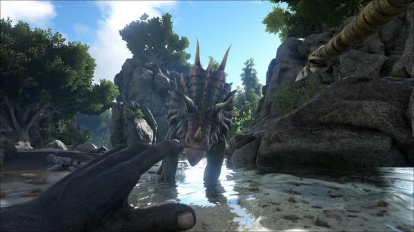 Screenshot from ARK: Survival Evolved showing a player reaching toward a Triceratops standing in shallow water amidst lush vegetation.