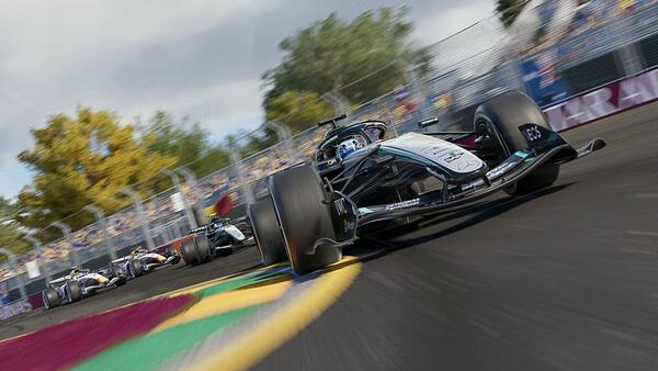 F1 25 screenshot: A race car speeds on a vibrant track, followed by other cars, with trees and spectators in the background.