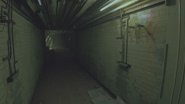Screenshot from ROUTINE showing a dimly lit, eerie corridor with scattered papers and overhead pipes along the walls.