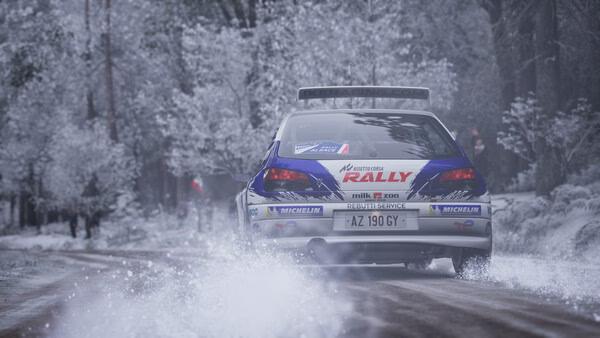 Screenshot from Assetto Corsa Rally shows a rally car speeding through a snowy forest track, kicking up snow behind it.