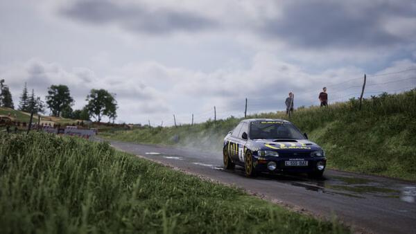 Assetto Corsa Rally screenshot: A rally car navigates a wet, narrow country road with spectators watching on a cloudy day.