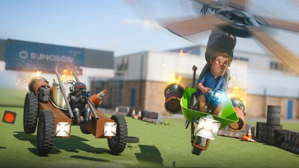 s&box screenshot: A player rides a green helicopter, while another drives a flaming vehicle in a grassy area with buildings nearby.