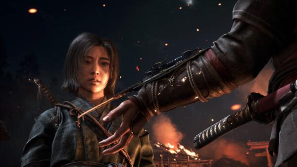 Screenshot from Assassin’s Creed Shadows: A figure extends a hand towards a person, with flames illuminating the dark scene.