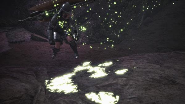 A screenshot from Monster Hunter: World showing a hunter investigating glowing monster tracks in a dark, rocky environment.