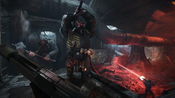 Screenshot from Warhammer 40,000: Darktide showing players battling a large armored enemy in a dimly lit, industrial environment.