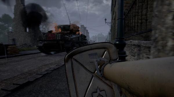 Screenshot from Hell Let Loose showing a soldier aiming an anti-tank weapon at a burning tank in a war-torn street.
