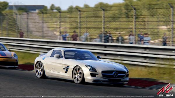 Assetto Corsa screenshot: A white sports car races down a sunny track, with spectators behind a fence watching intently.