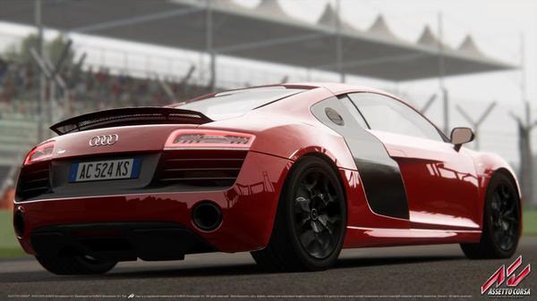 A red Audi R8 is parked on a racetrack in Assetto Corsa. The screenshot showcases its detailed design and realistic environment.