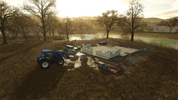 Farming Simulator 25 screenshot: A blue tractor beside a partially built structure on a farm, surrounded by trees and a river.