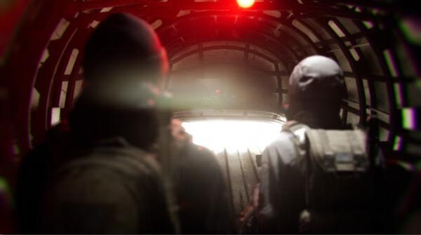 Screenshot from the game Bodycam showing two figures in tactical gear walking through a dimly lit tunnel with a red light overhead.