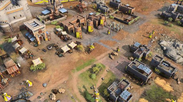 Age of Empires IV screenshot showing a medieval town with buildings, tents, and soldiers scattered across a grassy landscape.