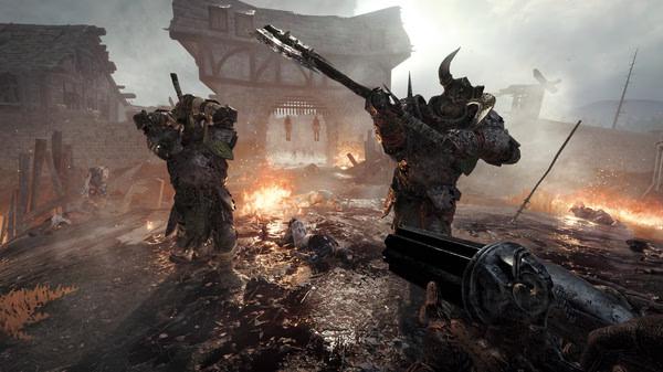Screenshot from Warhammer: Vermintide 2 showing players battling armored enemies in a fiery, war-torn village scene.