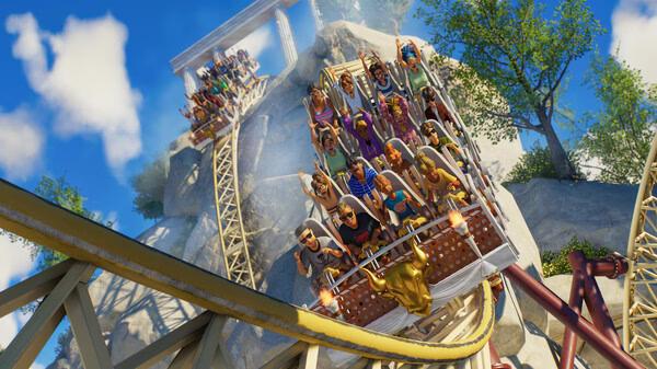 Planet Coaster 2 screenshot: A roller coaster full of excited riders descends a steep track against a backdrop of trees and clear skies.