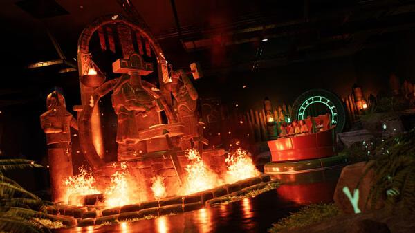Planet Coaster 2 screenshot: A fiery ride surrounded by ancient statues and glowing lights in a dark-themed setting.