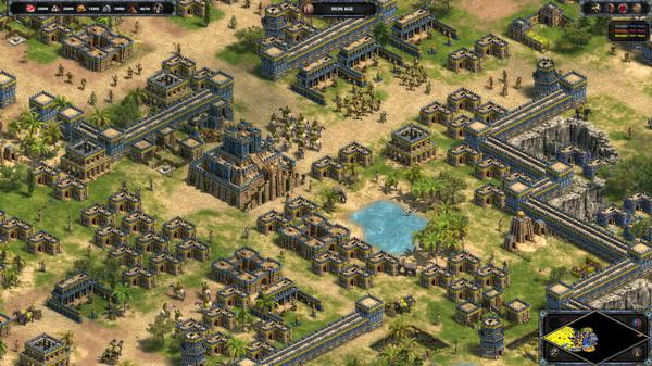 Age of Empires Definitive Edition screenshot showing a sprawling ancient city with a central temple, soldiers, and a small lake.