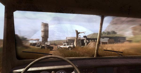 Far Cry 2 screenshot: View from inside a vehicle showing a dusty, rural landscape with buildings and parked cars outside.