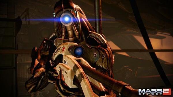 A "Mass Effect 2" screenshot showing a Geth holding a futuristic weapon, glowing blue lights visible on its face.