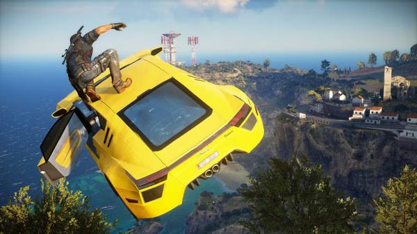 Just Cause 3 screenshot: Character rides a yellow sports car soaring over a coastal landscape with villages and radio towers.