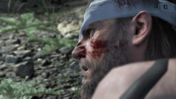 Screenshot from Metal Gear Solid V: The Phantom Pain showing a close-up of a character's face near a grassy, rocky terrain.